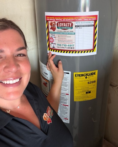 Loyalty team member beside a newly installed tank water heater with a Loyalty service log sticker on the tank