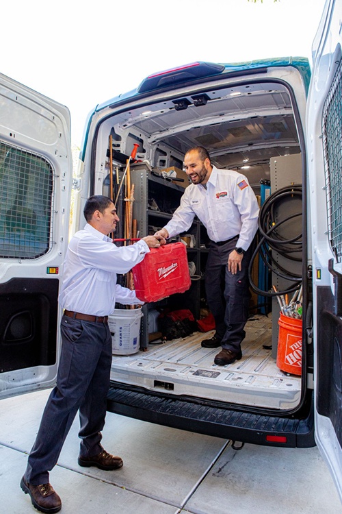 Two plumbers exchanging tools in a service van, showcasing professional plumbing equipment and a clean workspace, emphasizing Loyalty Plumbing's commitment to quality service.