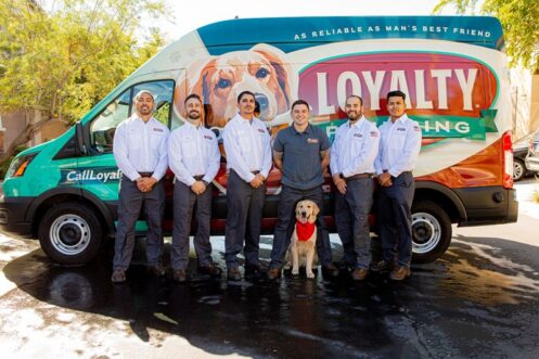 Team of plumbers from Loyalty Plumbing posing in front of their branded service van, featuring a friendly dog, emphasizing community and reliable plumbing services in Las Vegas.